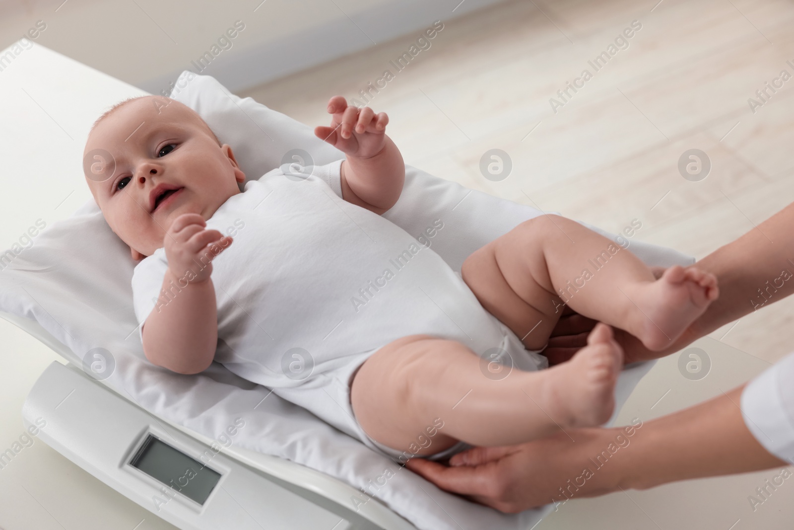 Photo of Pediatrician weighting cute little baby in clinic, closeup