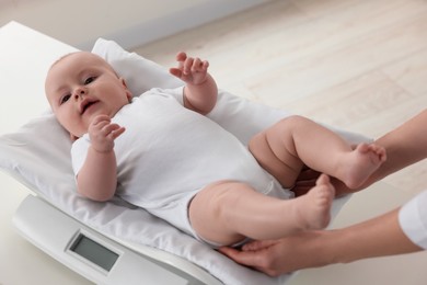 Photo of Pediatrician weighting cute little baby in clinic, closeup