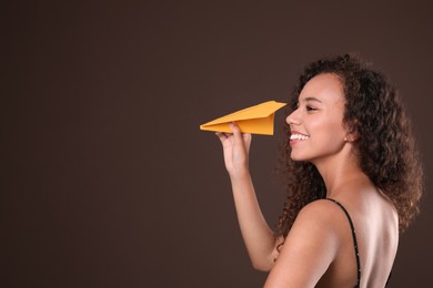 Beautiful African-American woman playing with paper plane on brown background. Space for text