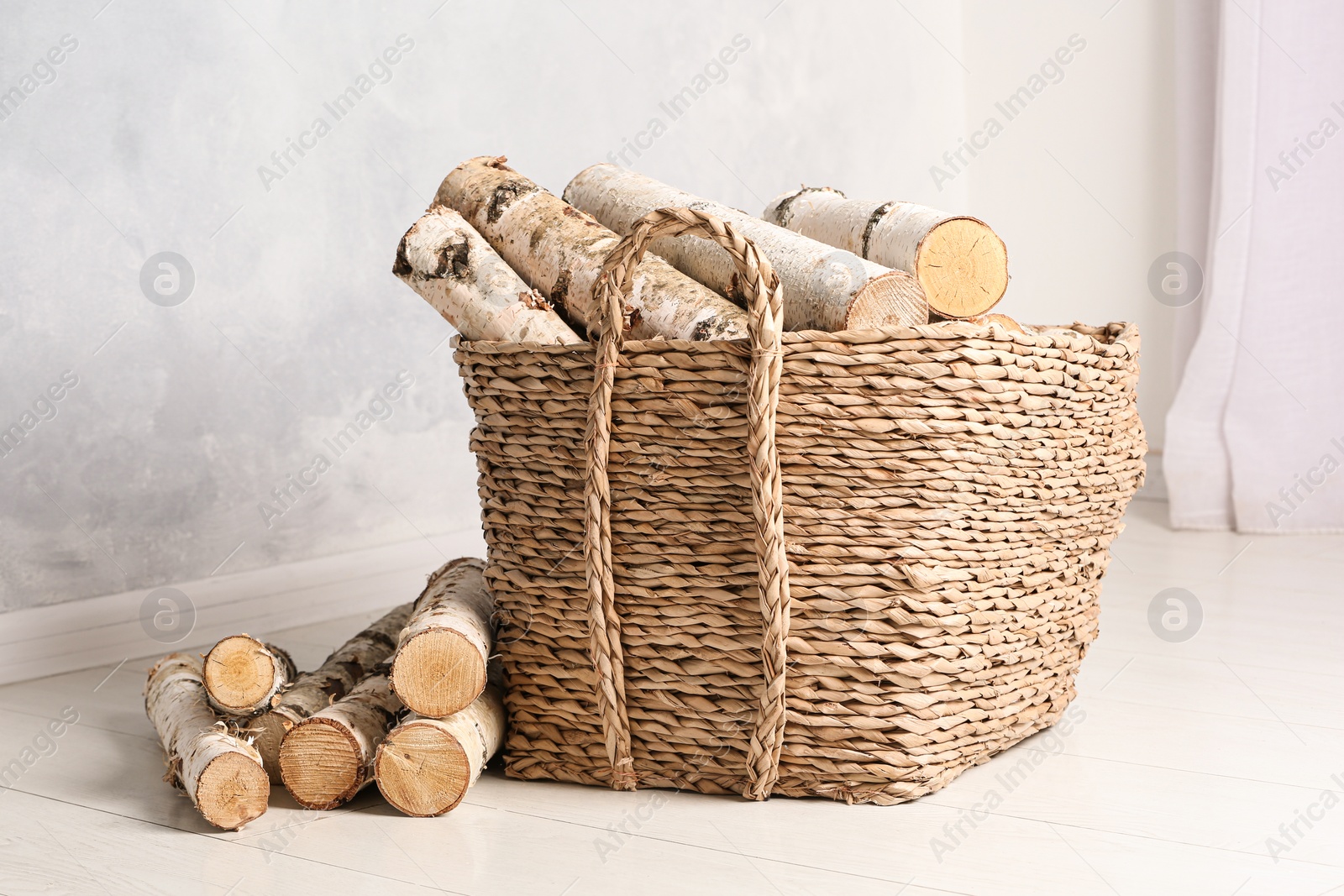 Photo of Wicker basket with cut firewood on white floor indoors