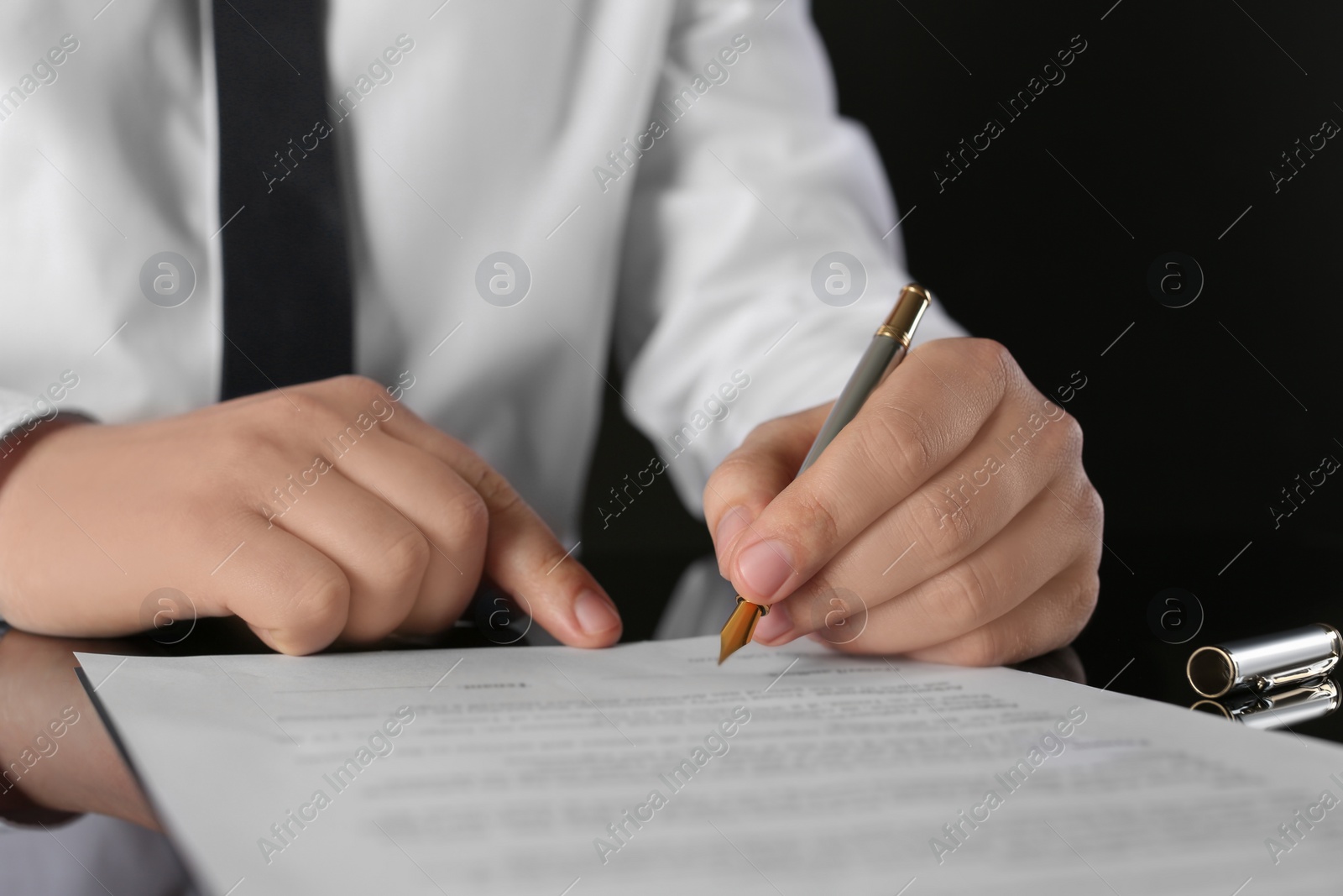 Photo of Notary signing document at black table, closeup