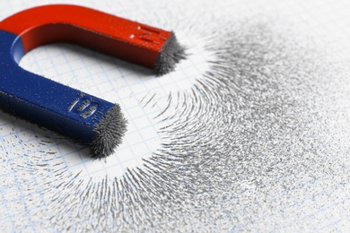Photo of Magnet attracting iron powder on squared paper, closeup