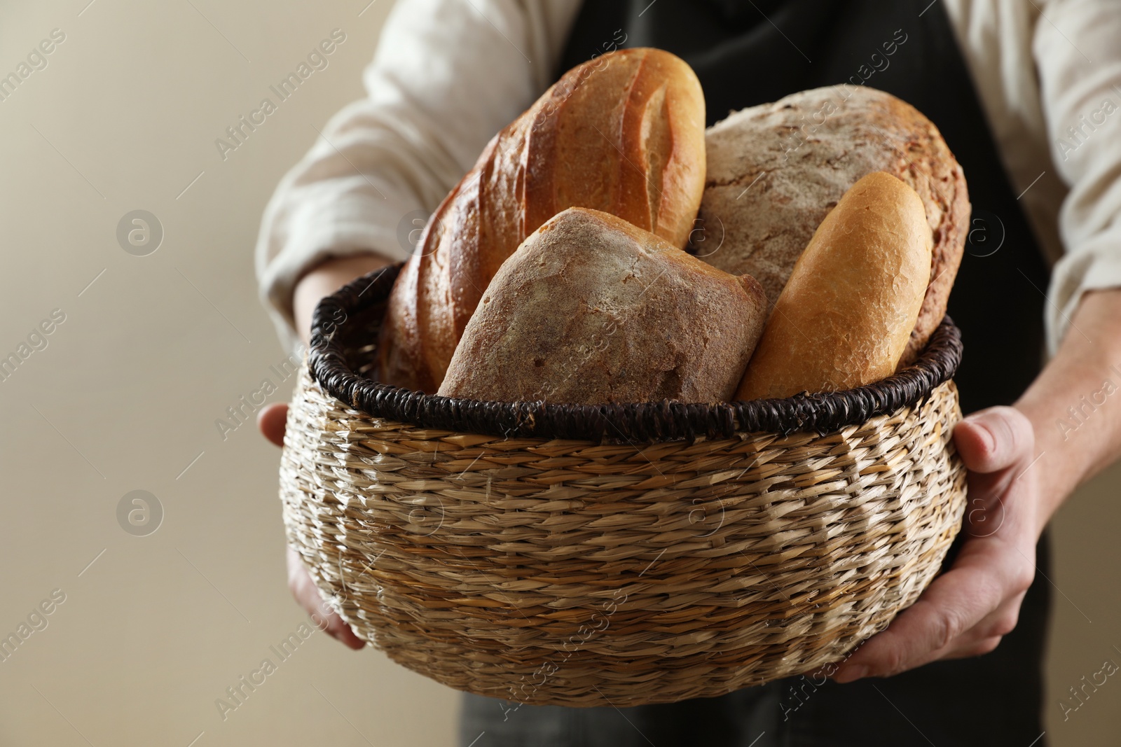 Photo of Man holding wicker basket with different types of bread on beige background, closeup