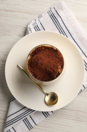 Photo of Delicious tiramisu in glass and spoon on white wooden table, top view