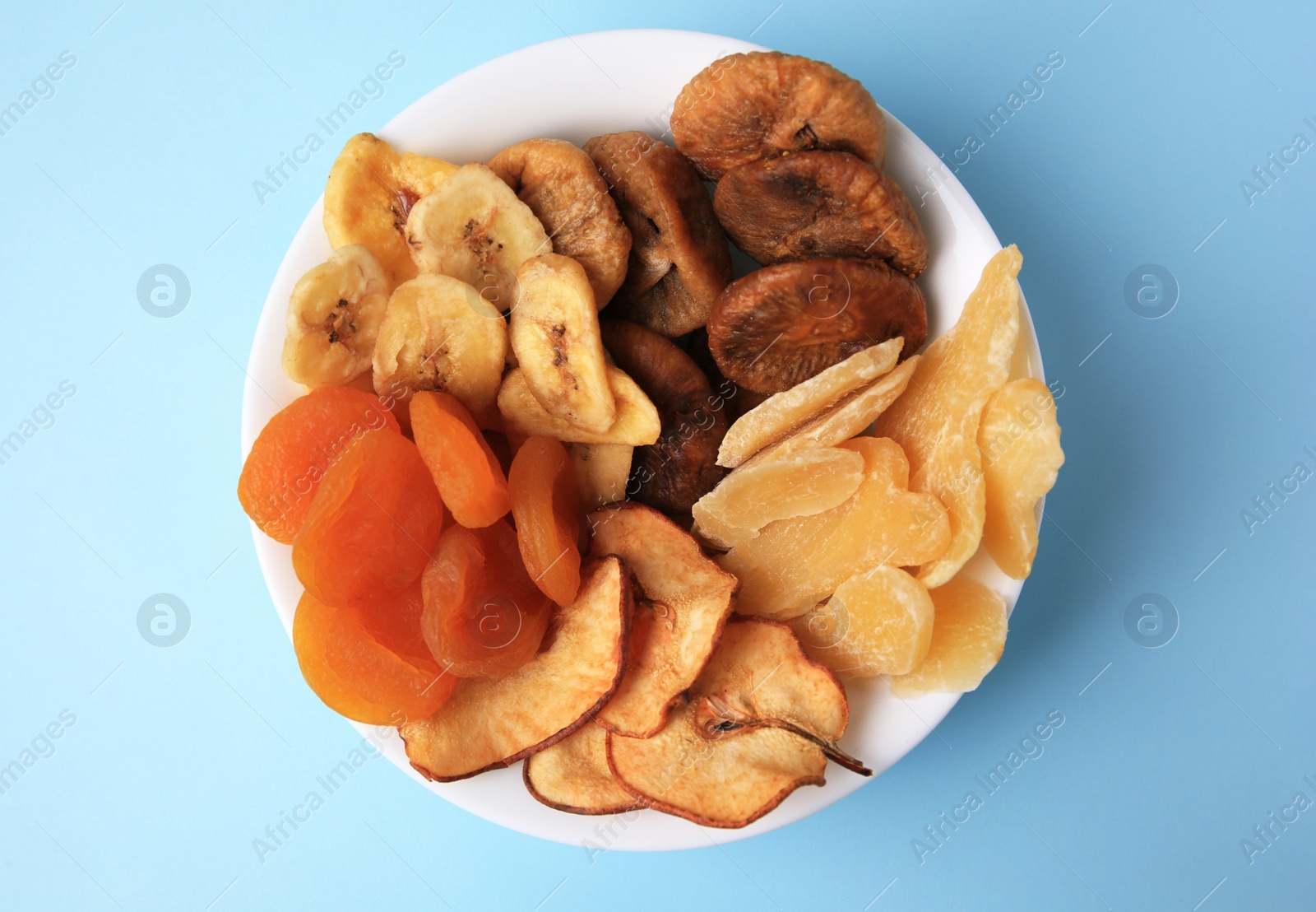 Photo of Bowl with different dried fruits on light blue background, top view
