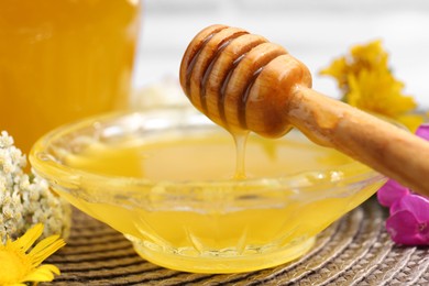 Photo of Delicious honey flowing down from dipper into bowl on wicker mat, closeup