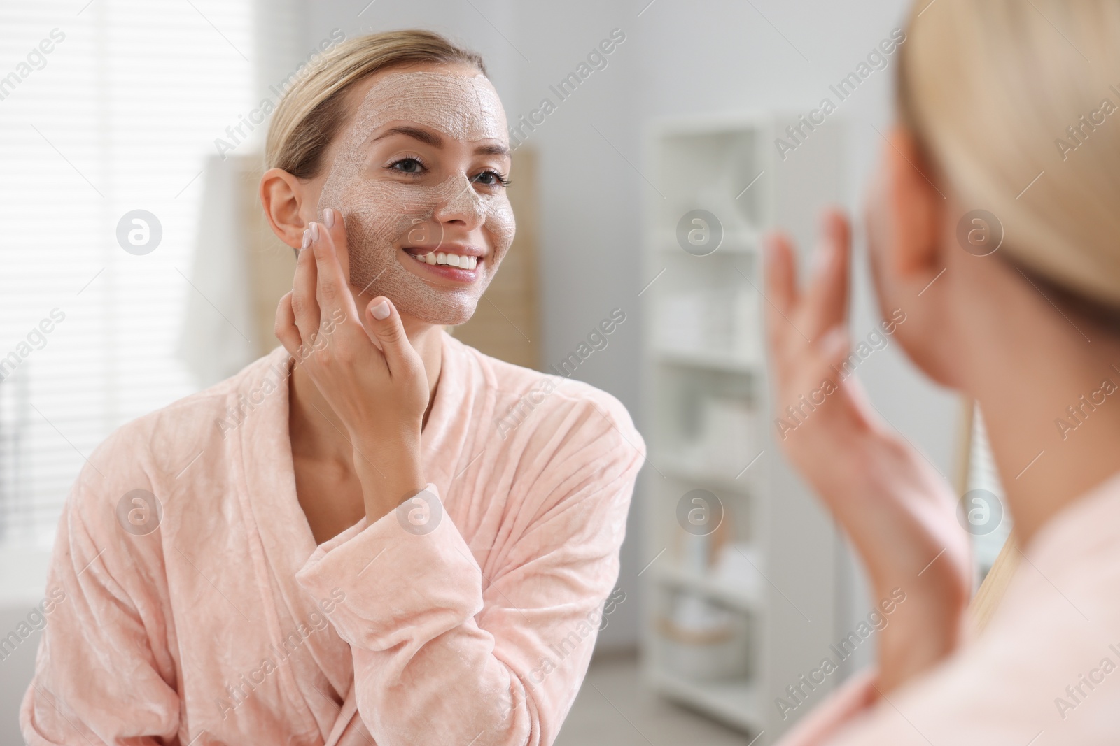 Photo of Woman applying face mask near mirror in bathroom. Spa treatments