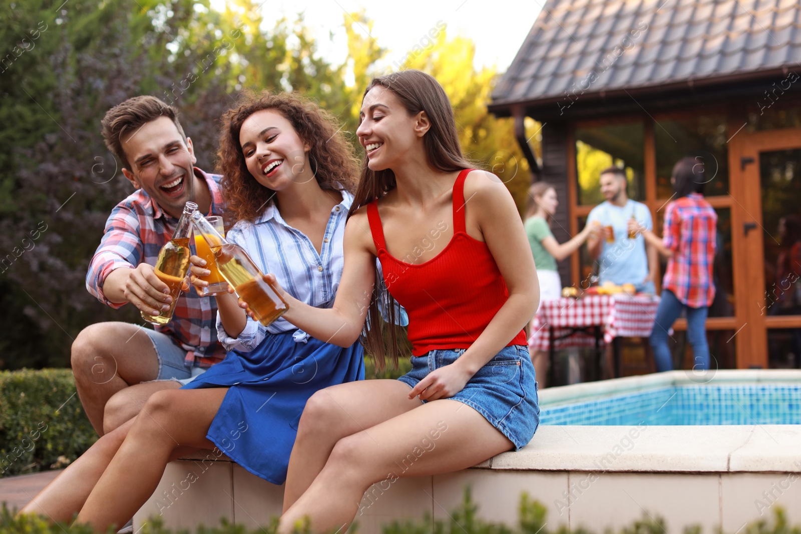 Photo of Happy friends with drinks at barbecue party near swimming pool outdoors