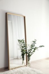 Photo of Large mirror with wooden frame near white wall in light room