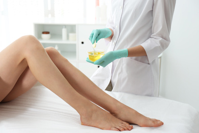 Photo of Woman getting wax epilation of legs in salon, closeup