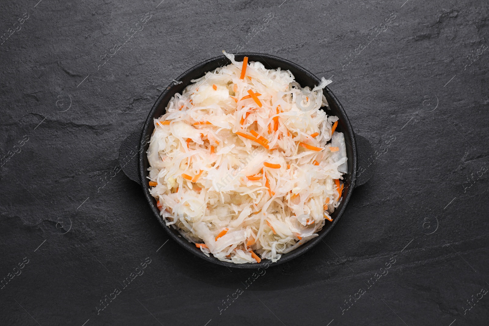 Photo of Bowl of tasty sauerkraut on black table, top view