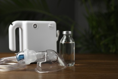 Modern nebulizer with face mask and liquid medicine on wooden table indoors. Inhalation equipment