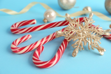 Photo of Christmas candy canes and decorative snowflake on light blue background, closeup