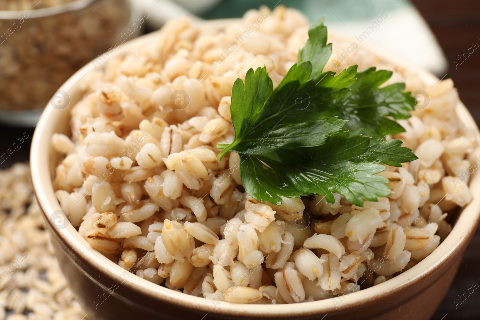 Photo of Delicious pearl barley with parsley in bowl on table, closeup