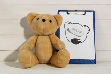 Photo of Clipboard with word Dyslexia and teddy bear on white wooden table