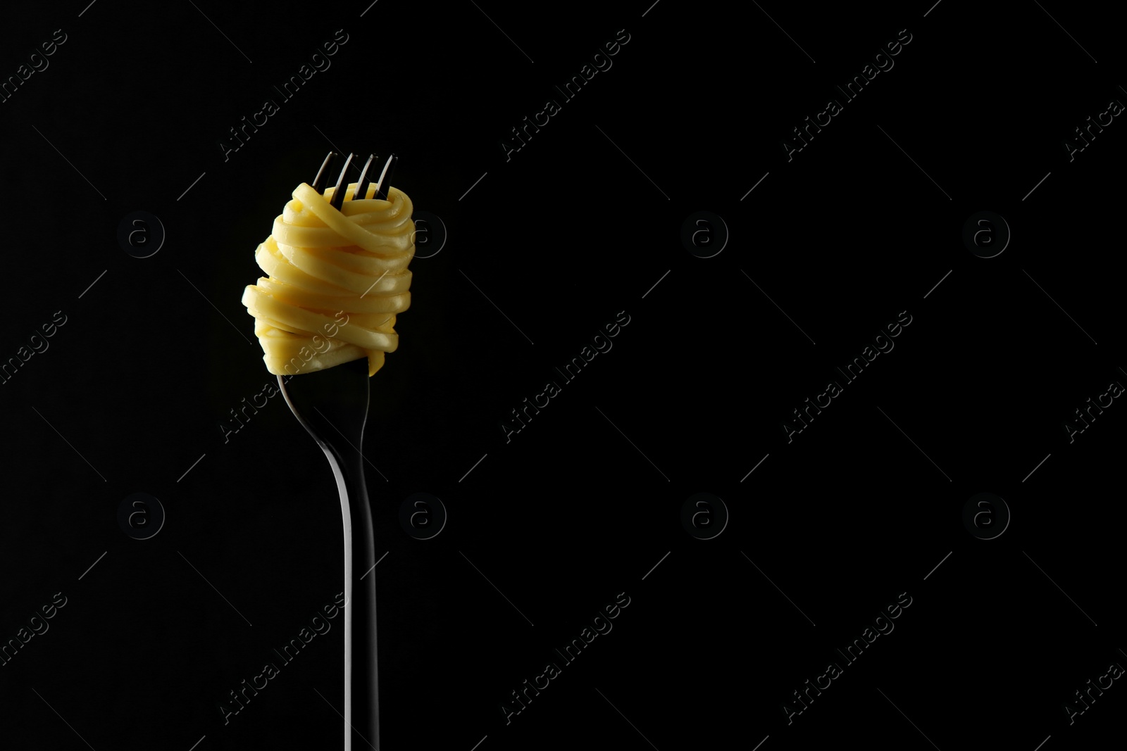 Photo of Fork with tasty pasta on black background, space for text