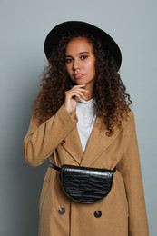 Beautiful African American woman with stylish waist bag on grey background