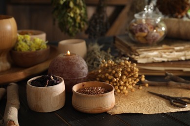 Photo of Different dry herbs, flowers, burning candle and flax seeds on black wooden table indoors