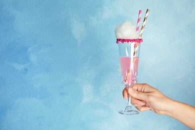 Photo of Woman holding glass with cocktail and candy cotton on color background, closeup. Space for text