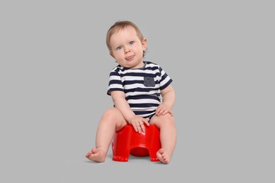 Photo of Little child sitting on baby potty against light grey background