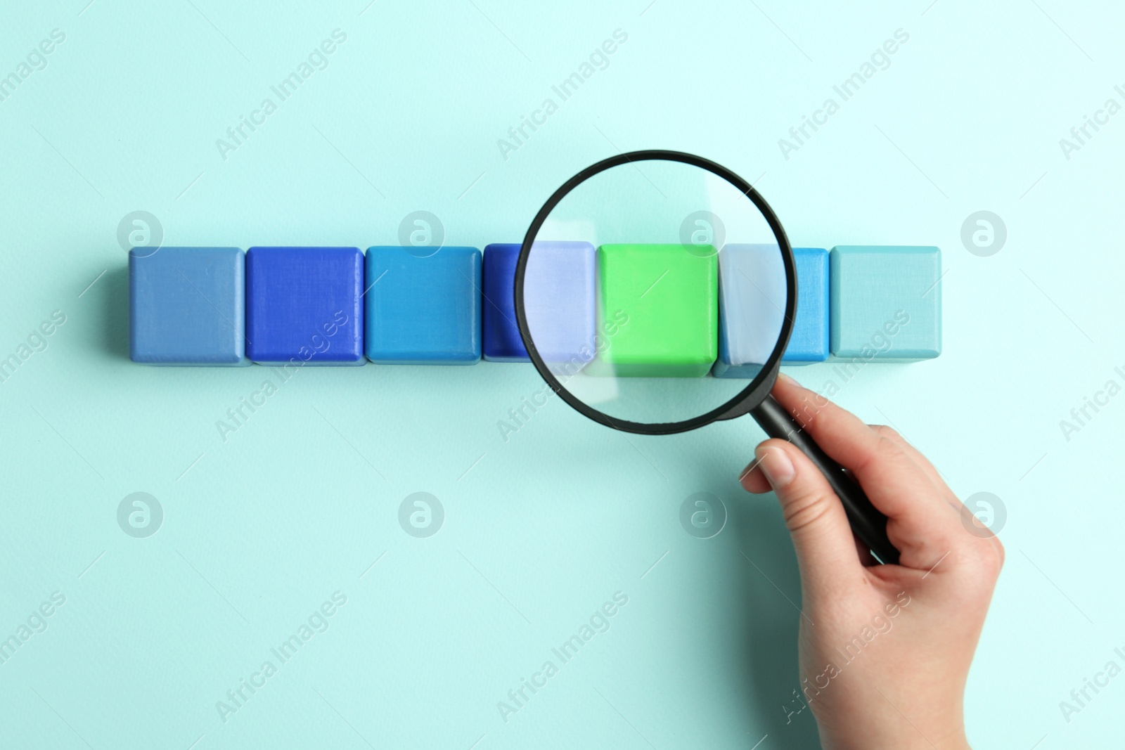 Photo of Woman holding magnifying glass above colorful cubes on light blue background, top view. Search concept