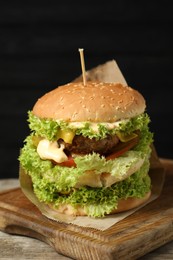 Photo of Burger with delicious patty on wooden table against dark background