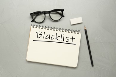Image of Word Blacklist written in notepad, pencil, eyeglasses and eraser on grey table, flat lay