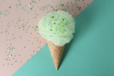 Sweet cotton candy in waffle cone on color background, top view