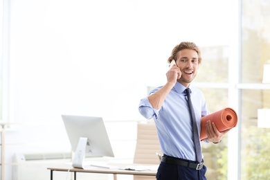 Photo of Young handsome businessman holding yoga mat in office. Space for text