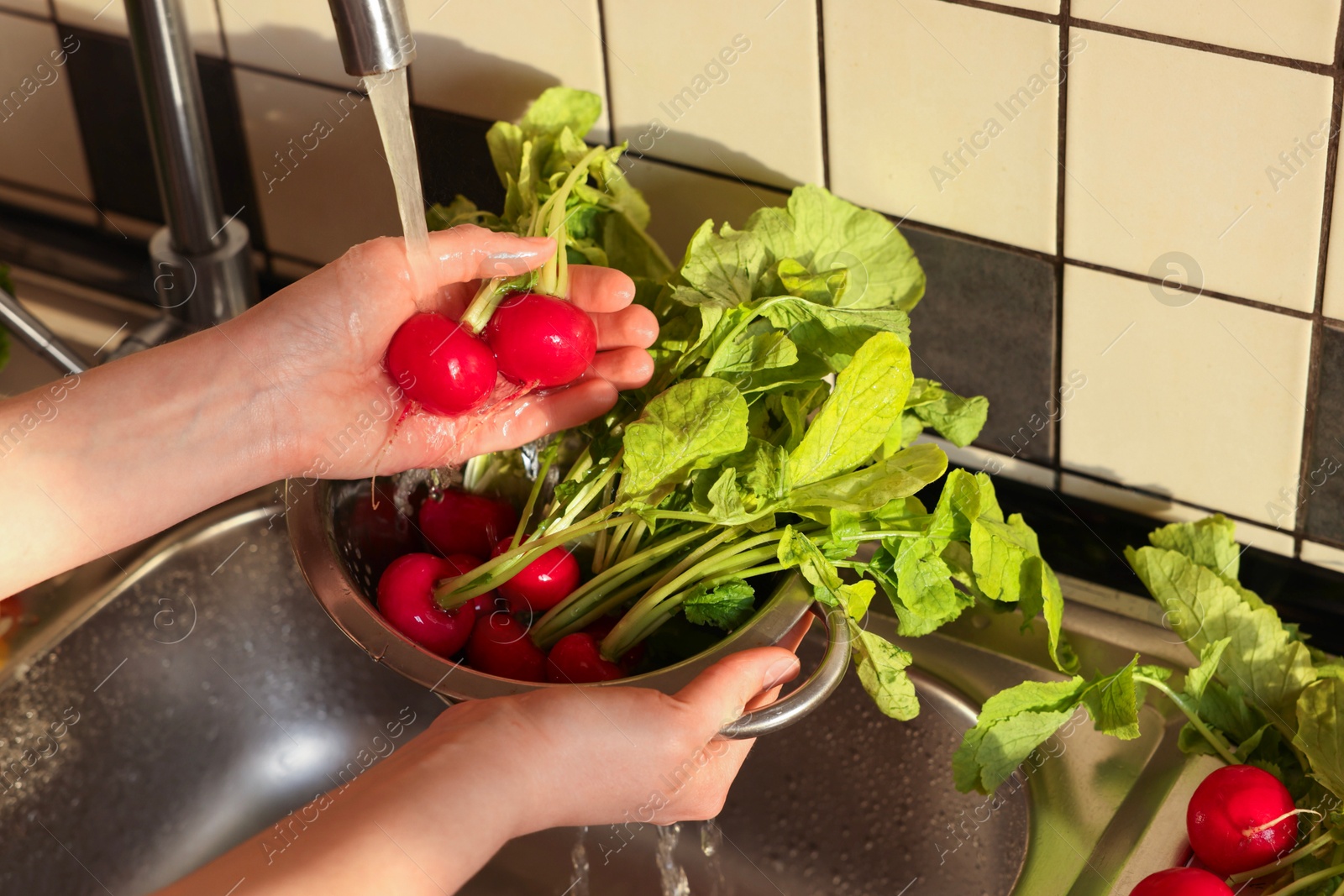 Photo of Woman washing fresh radishes in metal colander, closeup