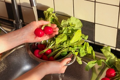 Photo of Woman washing fresh radishes in metal colander, closeup