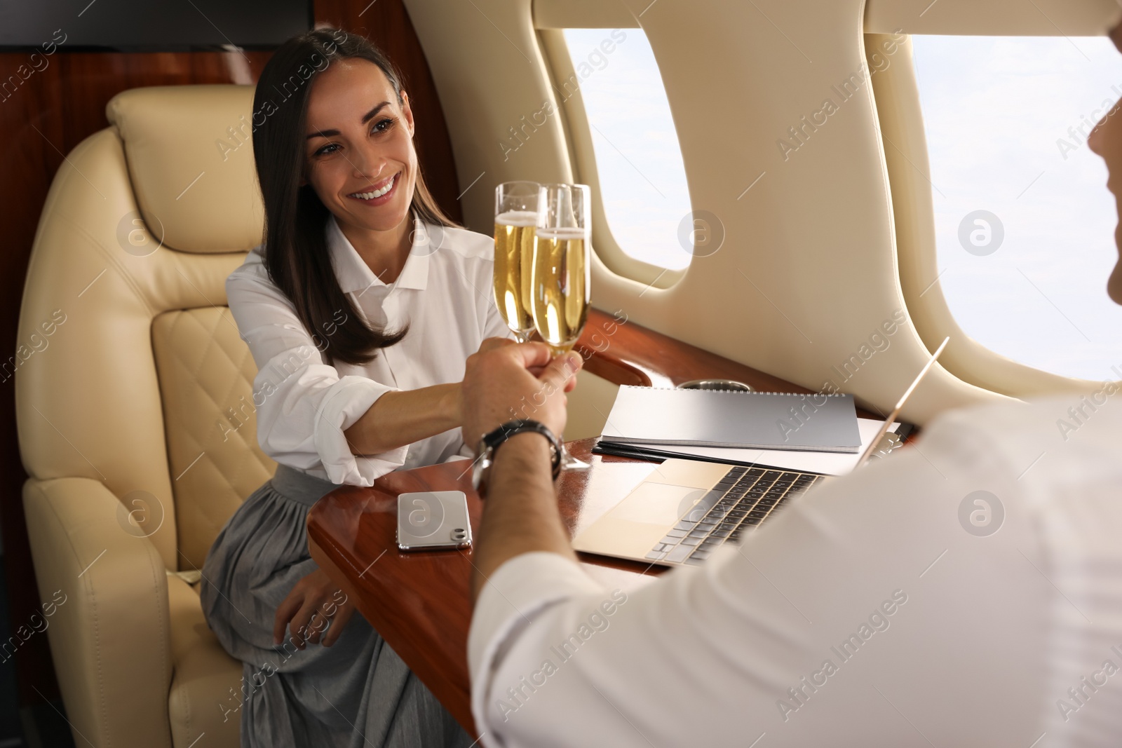 Photo of Colleagues clinking glasses of champagne at table in airplane during flight