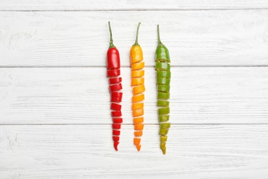 Different cut chili peppers on white wooden table, flat lay