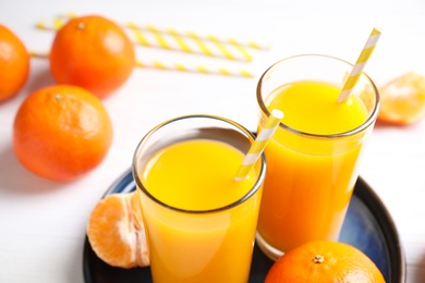 Glasses of fresh tangerine juice and fruits on white table
