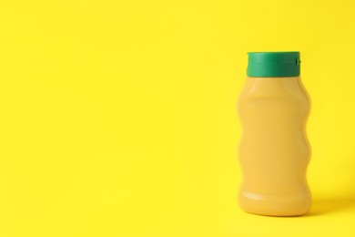 Spicy mustard in plastic bottle on yellow background, space for text