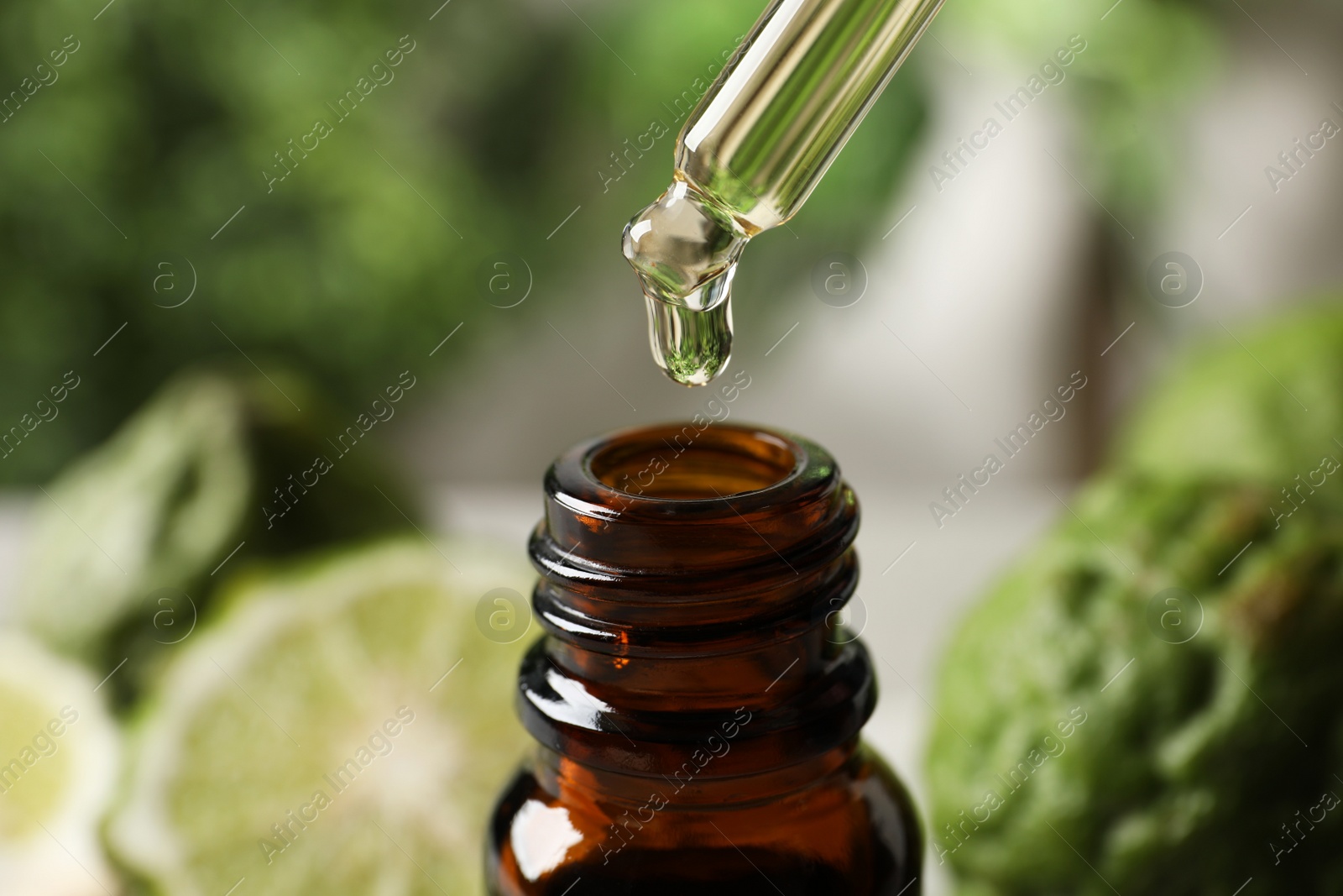 Photo of Dripping bergamot essential oil into glass bottle against blurred background, closeup