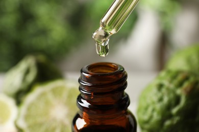 Photo of Dripping bergamot essential oil into glass bottle against blurred background, closeup