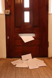 Wooden door with mail slot and many envelopes indoors