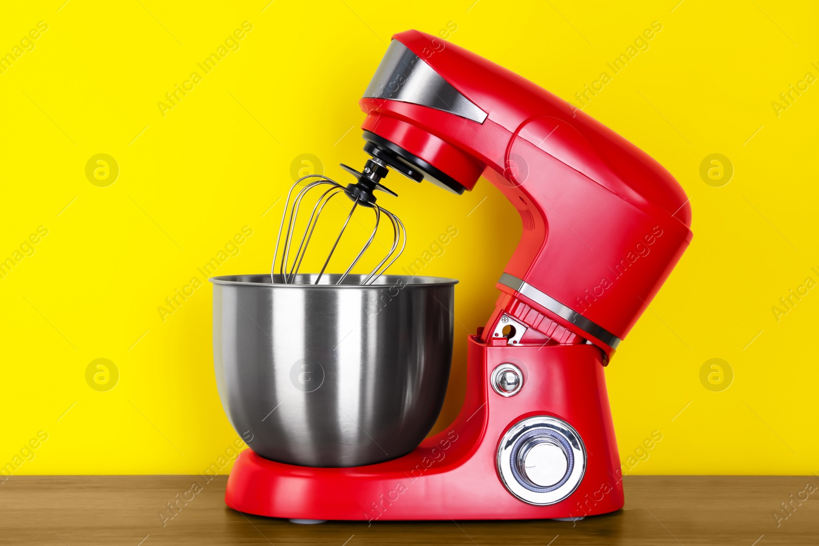 Photo of Modern red stand mixer on wooden table against yellow background