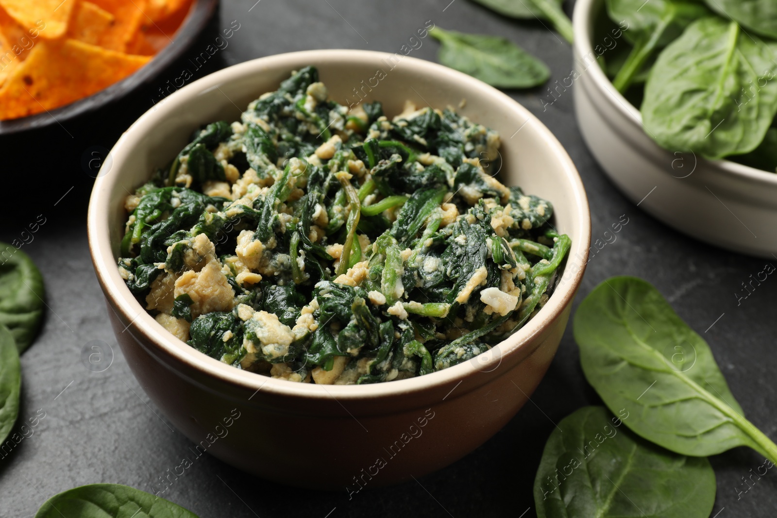 Photo of Tasty spinach dip with egg in bowl on black table, closeup