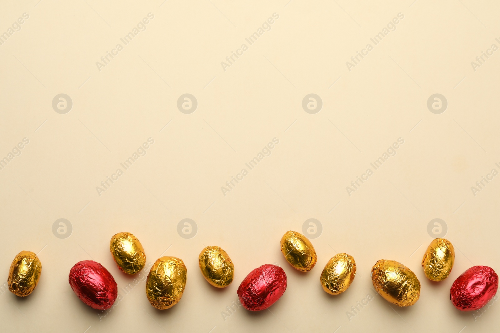 Photo of Chocolate eggs wrapped in red and golden foil on beige background, flat lay. Space for text