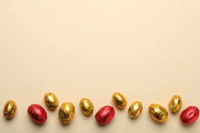 Photo of Chocolate eggs wrapped in red and golden foil on beige background, flat lay. Space for text