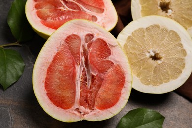 Fresh cut pomelo fruits with green leaves on dark table, closeup