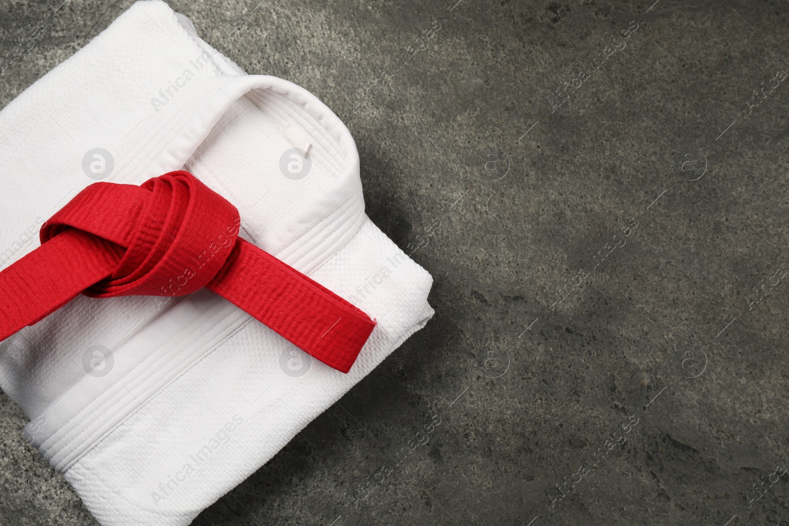 Photo of Red karate belt and white kimono on gray textured background, top view. Space for text