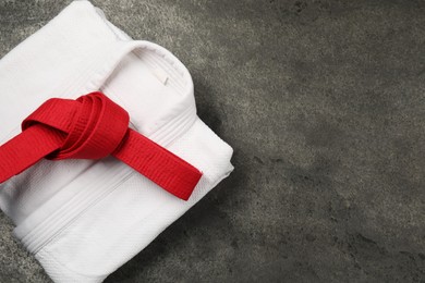 Red karate belt and white kimono on gray textured background, top view. Space for text