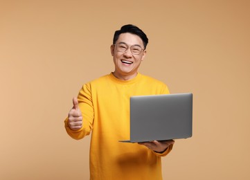 Photo of Smiling man with laptop showing thumb up gesture on beige background