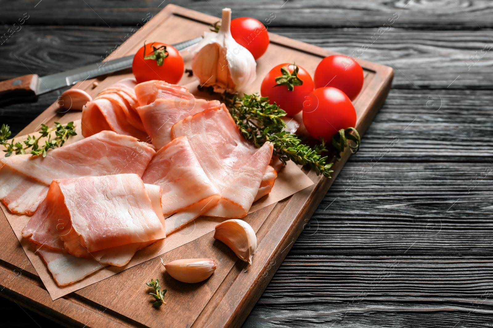 Photo of Board with raw bacon rashers, tomatoes and garlic on wooden background