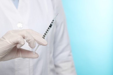 Doctor holding syringe on light blue background, closeup. Space for text