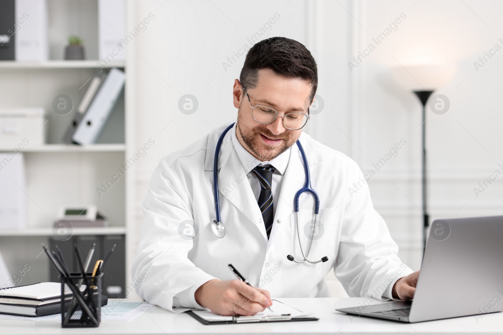 Photo of Smiling doctor having online consultation via laptop at table in clinic