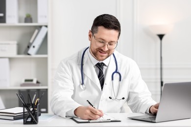 Smiling doctor having online consultation via laptop at table in clinic